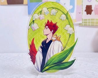 May include: An oval acrylic standee featuring an anime-style character with red hair and fox ears, wearing a white and black outfit. The character is surrounded by white lily of the valley flowers and green leaves against a light green grid background.