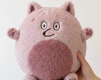May include: A round, plush stuffed animal in a light pink color with a darker pink circular patch on the belly. It features two small ears, embroidered circular eyes, a simple curved mouth, and two small arms and legs with dark pink paw prints.