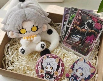 May include: A plush doll with light gray hair and yellow eyes, a circular pinback button, an acrylic charm, and a set of trading cards featuring a character with long hair and a dark mask, all arranged inside a cardboard box with paper filler.