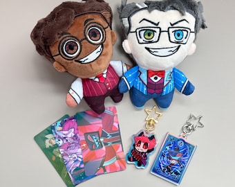 May include: Two plush dolls with smiling faces, glasses, and formal attire, alongside character keychains and colorful cards. The dolls are brown and white, and the keychains have star-shaped attachments. The cards feature various character designs.