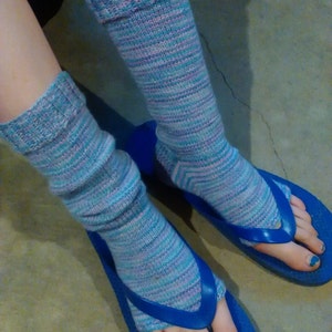 May include: A pair of blue flip-flops with blue and purple striped knit socks. The socks are folded over at the top. The person's toenails are painted blue.