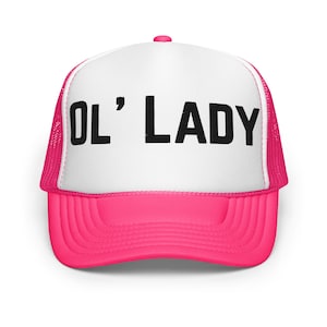 May include: A trucker hat with a white front panel and a bright pink brim and mesh back. The text "OL' LADY" is printed in bold black letters across the front of the hat.