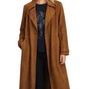 May include: A long, brown suede coat with a notched collar, button closure, and pockets. The coat is knee-length and has long sleeves with buttoned cuffs. The coat is a solid color and appears to be made of a soft material.