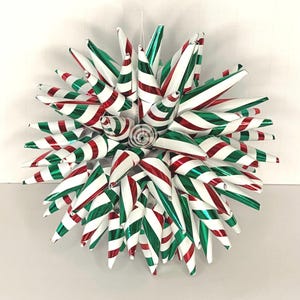 May include: A festive, star-shaped Christmas ornament. The ornament is composed of numerous cone-shaped elements in alternating red, white, and green stripes. The design is symmetrical, with a central spiral detail. The ornament is suspended by a thin, white string.