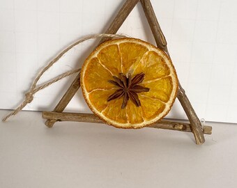 May include: A dried orange slice with a star anise centre, suspended within a triangular frame made of twigs. A natural twine loop is attached for hanging. The orange slice is approximately 7.6 cm in diameter.