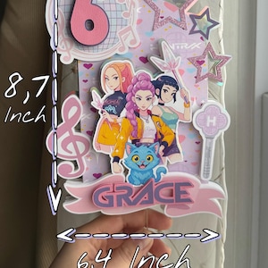 May include: A pink and white cake topper with the number 6, musical notes, and star accents. It features a cartoon illustration of three girls and a blue cat. The topper is 8.7 inches tall and 6.4 inches wide.