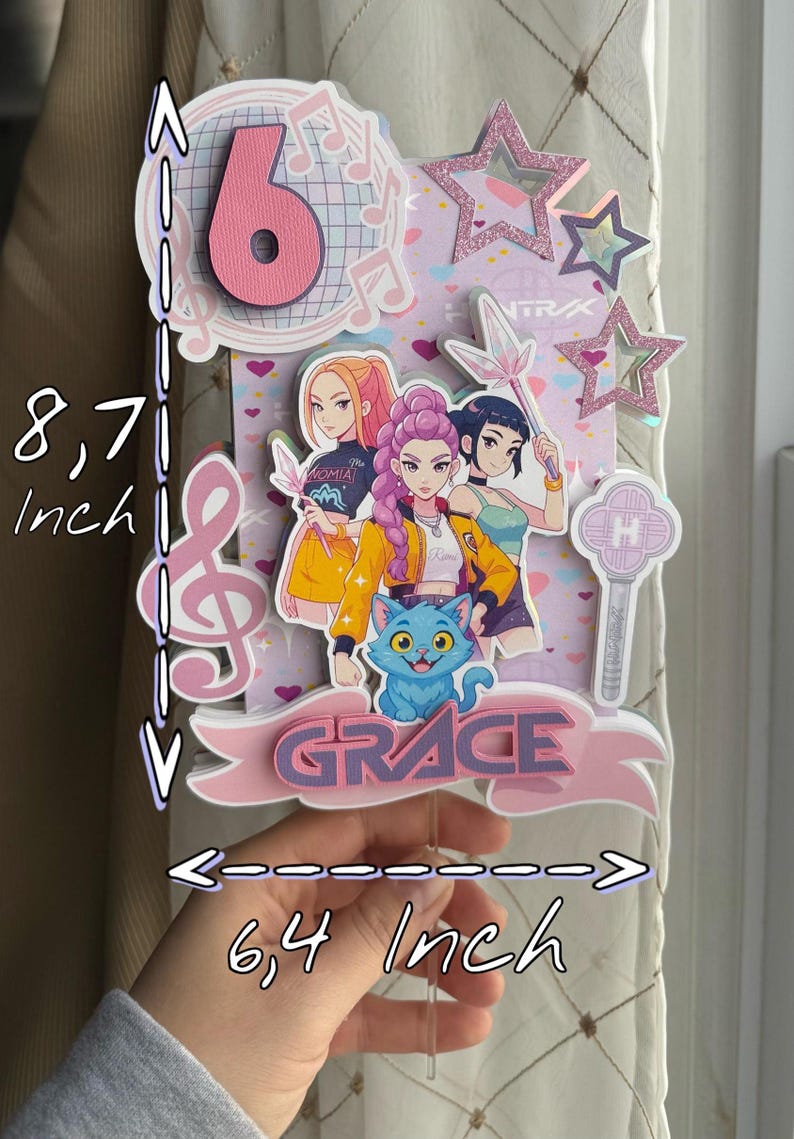 May include: A pink and white cake topper with the number 6, musical notes, and star accents. It features a cartoon illustration of three girls and a blue cat. The topper is 8.7 inches tall and 6.4 inches wide.