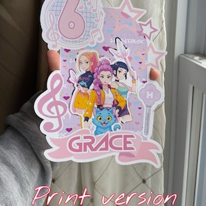May include: A pink and white birthday cake topper featuring a cartoon image of three girls, a blue cat, and the name "GRACE". The number 6 is displayed at the top, along with musical notes and stars. The words "Print version" are written in pink.