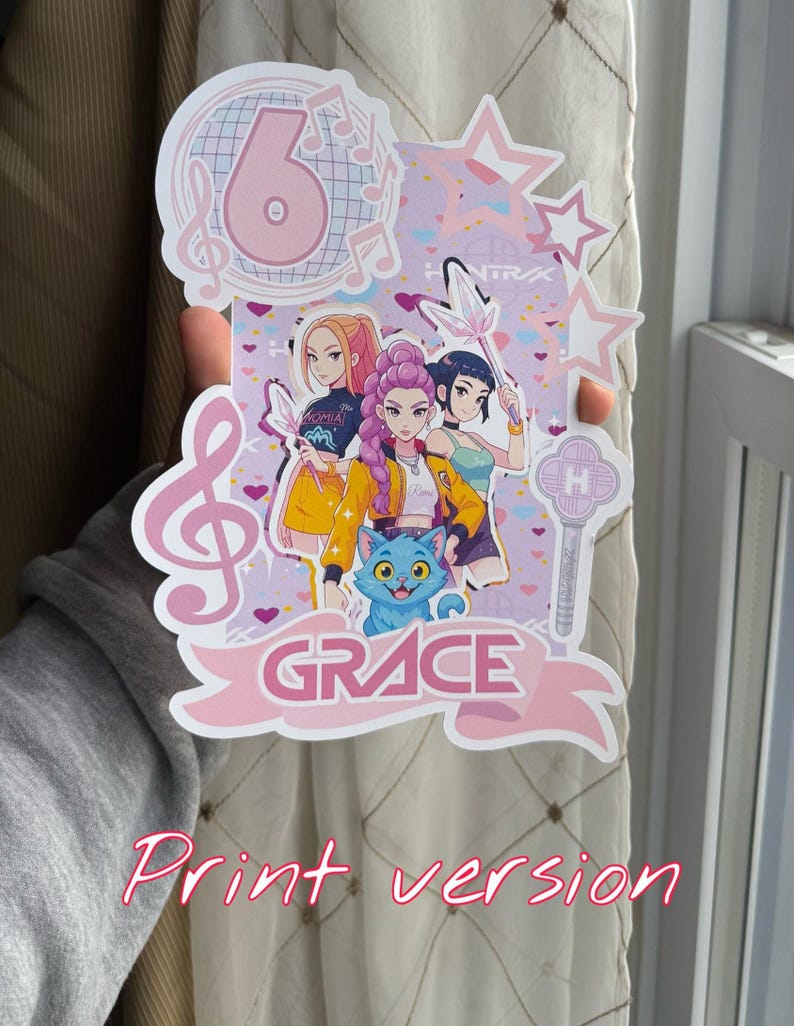 May include: A pink and white birthday cake topper featuring a cartoon image of three girls, a blue cat, and the name "GRACE". The number 6 is displayed at the top, along with musical notes and stars. The words "Print version" are written in pink.