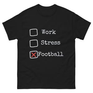 Może przedstawiać: Czarny t-shirt z białym tekstem i polami wyboru. Tekst brzmi "Work", "Stress" i "Football", z czerwonym "X" w polu "Football". Odzież codzienna.