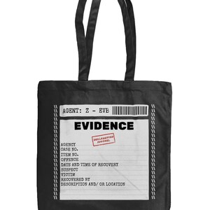 May include: A black tote bag featuring a white rectangular graphic printed on the front. The graphic resembles an evidence bag label with the text AGENT: Z - EVB, a barcode, the word EVIDENCE, and a red stamp reading DECLASSIFIED APPAREL.