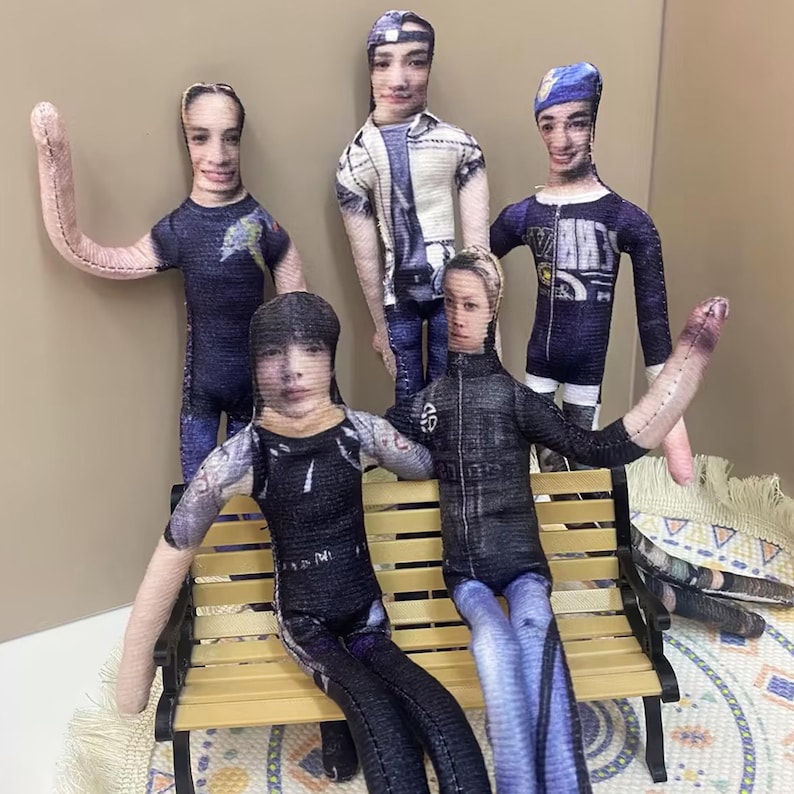 May include: Five handmade fabric dolls with printed faces and clothing. The dolls are posed in various positions, some standing and some seated on a miniature bench. The dolls' outfits include jackets, t-shirts, and jeans.