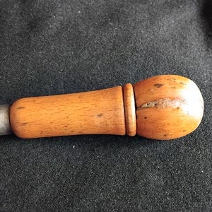May include: A hand tool with a smooth, light brown wooden handle that features a rounded, bulbous end and a cylindrical grip. A metallic, silver-coloured ferrule and a small, adjustable metal chuck are attached to the front of the wooden handle.
