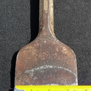 May include: A vintage, rusty metal chisel with a wide blade, measuring approximately 3 inches in length. The handle is stamped with the text "BEDFORD ENGLAND". The tool is placed on a dark surface.