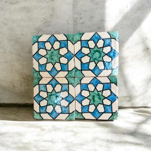 Peut inclure: Un ensemble de quatre carreaux de céramique carrés disposés en grille, chacun présentant un motif géométrique en étoile répétitif dans des tons de bleu sarcelle, bleu vif et blanc cassé, souligné par de fines lignes noires.