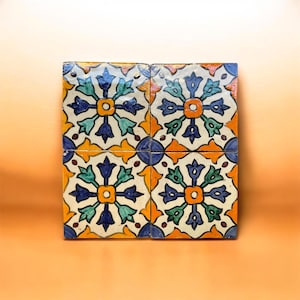 Peut inclure: Quatre carreaux de céramique carrés avec un motif floral. Les carreaux présentent un motif répétitif de fleurs bleues, vertes, jaunes et oranges sur un fond blanc. Les carreaux sont disposés en carré.