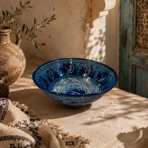 Peut inclure: Un bol en céramique rond arborant une glaçure bleu profond avec des motifs floraux et géométriques complexes peints à la main en blanc et bleu foncé. Le bol présente un bord large et ouvert ainsi qu'une finition lisse et brillante.