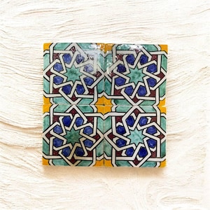 Peut inclure: Quatre carreaux de céramique carrés avec un motif géométrique répétitif. Le motif présente des formes bleues, vertes et bordeaux avec des contours blancs, sur une bordure jaune. Les carreaux sont disposés ensemble, créant un design cohérent.