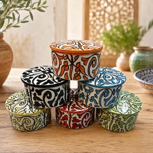 Peut inclure: Une pile de six pots en céramique ronds avec couvercles, ornés de motifs floraux et de volutes peints à la main dans des couleurs vives comme l'orange, le noir, le bleu, le rouge, le jaune et le vert. Chaque pot possède un couvercle assorti.