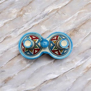 Puede incluir: Un plato doble de cerámica con borde y detalles en azul claro. El plato presenta dos compartimentos circulares con una esfera central. Cada compartimento tiene un colorido patrón geométrico en rojo, amarillo, verde y azul. El plato está sobre una superficie de mármol.