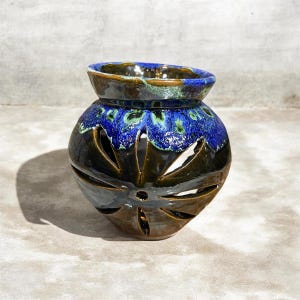 Peut inclure: Un vase en céramique fait à la main avec un design unique. Le vase présente une base marron foncé avec des motifs découpés et un dessus émaillé bleu et vert vif. Le vase est une pièce décorative.
