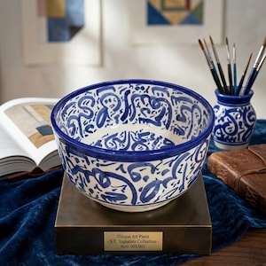 Peut inclure: Un bol en céramique blanc et bleu avec un motif abstrait. Le bol est posé sur un socle en bronze, avec un vase assorti et des pinceaux en arrière-plan. Le texte sur la base indique "Unique Art Piece - S.E. Signature Collection - Item 001/001."