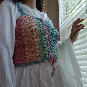 May include: A crocheted top with a rainbow colour pattern and a lace-up front. The top is made with a textured stitch and has a fitted silhouette.