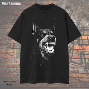 May include: Black t-shirt featuring a black and white graphic of a snarling Doberman Pinscher. The text "VISESTUDIOS" is at the top left. The text "THIS COLOUR IS BLACK" is at the bottom left.