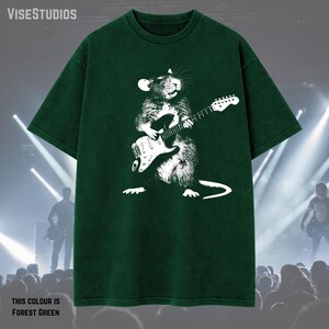May include: Forest green t-shirt featuring a white graphic of a rat playing an electric guitar. The text "VISESTUDIOS" is at the top left. The text "THIS COLOUR IS FOREST GREEN" is at the bottom left.