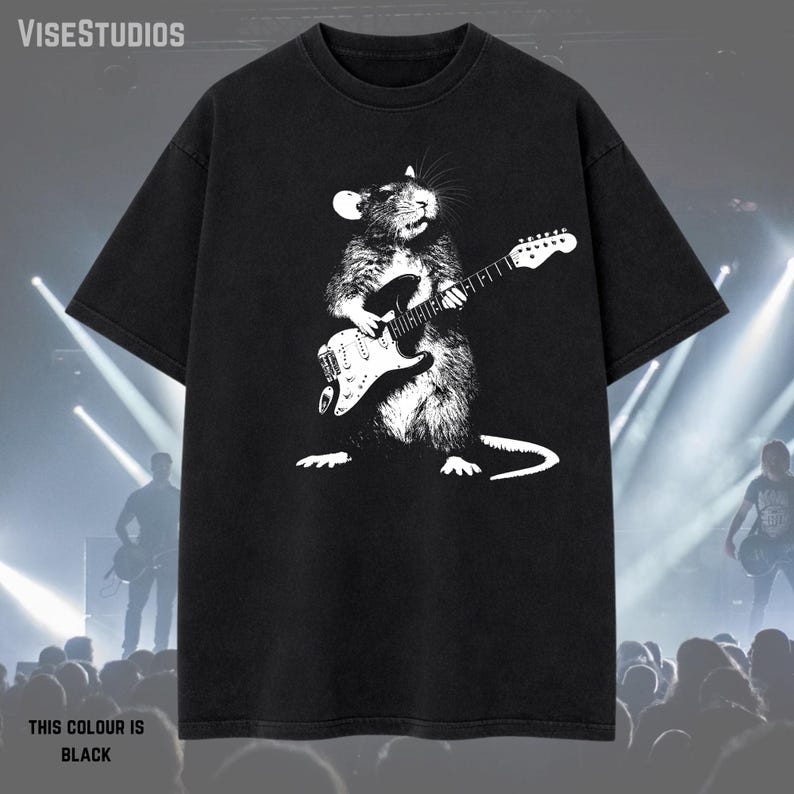 May include: Black t-shirt featuring a white graphic of a rat playing an electric guitar. The text "THIS COLOUR IS BLACK" is at the bottom. The brand name "VISESTUDIOS" is at the top. The shirt is a crew neck.