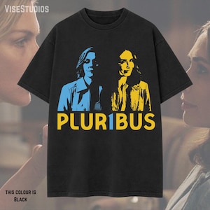 May include: Black t-shirt featuring a blue and yellow graphic of two people and the word "PLUR1BUS" in yellow. The text "THIS COLOUR IS BLACK" is at the bottom. The brand name "VISESTUDIOS" is at the top.