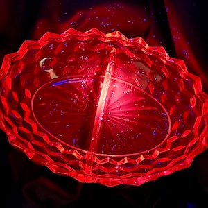 Könnte beinhalten: Eine leuchtend rote, geteilte Glasservierschale. Die Schale hat ein geometrisches, rautenförmiges Muster am Rand und einen Mittelsteg. Die ovale Schale scheint aus Kristall oder einem ähnlichen Material zu bestehen.