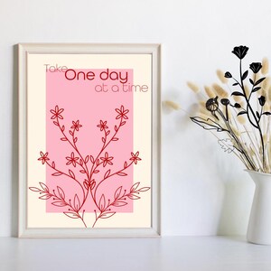 Puede incluir: Impresión artística enmarcada con un fondo crema y una forma rectangular rosa. El arte lineal floral rojo está centrado en la forma rosa. El texto "Take One day at a time" está impreso en rojo. Un jarrón blanco con flores secas está a la derecha.