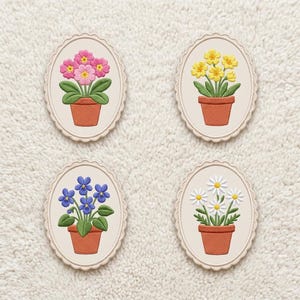 Op de afbeelding: Vier geborduurde bloemmotieven in ovale frames. Elk heeft een andere bloem in een terracotta pot: roze sleutelbloemen, gele narcissen, blauwe viooltjes en witte madeliefjes. De frames hebben een geschulpte rand.