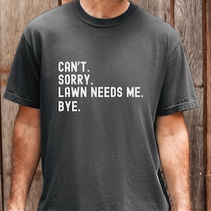 May include: A dark gray t-shirt with the text "CAN'T. SORRY. LAWN NEEDS ME. BYE." in white. The shirt has a crew neck and short sleeves. The word "Pepper" is in the bottom right corner.