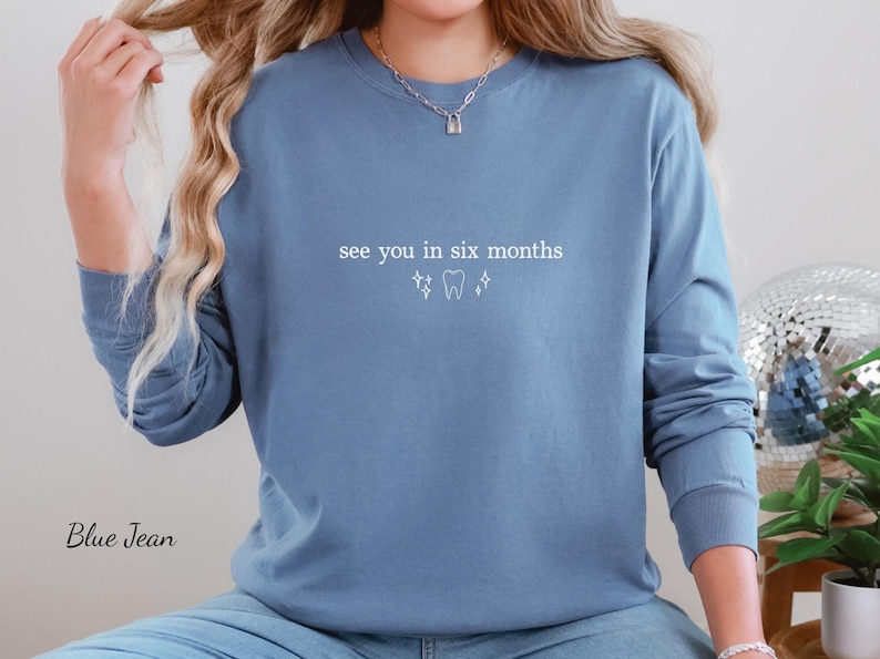 K&ouml;nnte beinhalten: Blaues Langarm-Sweatshirt mit dem Text "see you in six months" und einer Zahn-Grafik in Wei&szlig;. Das Sweatshirt hat eine einfarbige blaue Farbe. Der Text und die Grafik sind mittig auf der Brust platziert.