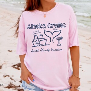 May include: Light pink t-shirt with a navy blue graphic that reads "Alaska Cruise 2026" with a ship, whale tail, and cocktail illustration. The text "making memories" and "Smith Family Vacation" are also included.