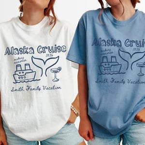 May include: Two short-sleeved t-shirts, one white and one blue, each with a navy blue graphic. The graphic includes the text "Alaska Cruise 2026", a ship, a whale tail, and a cocktail. The text "Smith Family Vacation" is also included.
