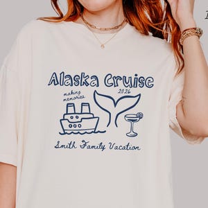 May include: Ivory-colored t-shirt with a navy blue graphic that reads "Alaska Cruise 2026". The design includes a ship, whale tail, and cocktail. The text "making memories" and "Smith Family Vacation" are also included.