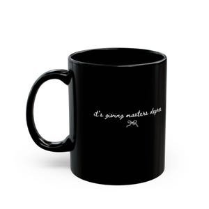 Puede incluir: Taza de caf&eacute; de cer&aacute;mica negra con asa curva. La taza presenta la frase "it's giving masters degree" en escritura blanca, acompa&ntilde;ada de un peque&ntilde;o lazo. Ideal para bebidas calientes.