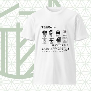 以下が含まれることがあります： 日本語のアイコンとテキストが黒でプリントされた白い半袖Tシャツ。デザインには、トイレ、電車、タクシー、バス停、ゴミ箱、ラーメン、ロッカー、コンビニエンスストアのシンボルと、それに対応する日本語のテキストが含まれています。
