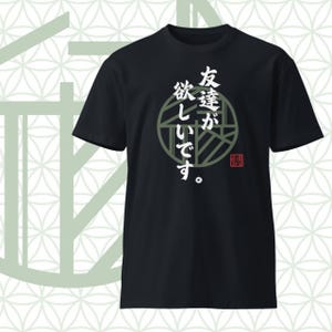 以下が含まれることがあります： 黒の半袖Tシャツ。ダークグリーンの幾何学模様が描かれた円形のグラフィックが中央に配置されています。円の上には白い日本語のテキスト「友達が欲しいです」が書かれています。右下には黒い文字が入った小さな赤い四角いスタンプが押されています。