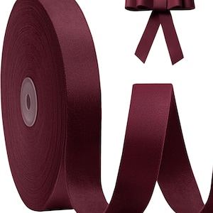 May include: A large spool of deep burgundy ribbon with a matte, fabric-like texture. The ribbon is wound tightly around a central core, with a loose end extending outward. A separate, pre-tied bow made from the same burgundy ribbon is shown.