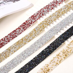 May include: Five parallel strips of decorative trim, each covered in small, reflective rhinestones. The colors include red, gold, silver, black, and a mix of white and gold. Each strip features a dense, uniform arrangement of faceted stones.