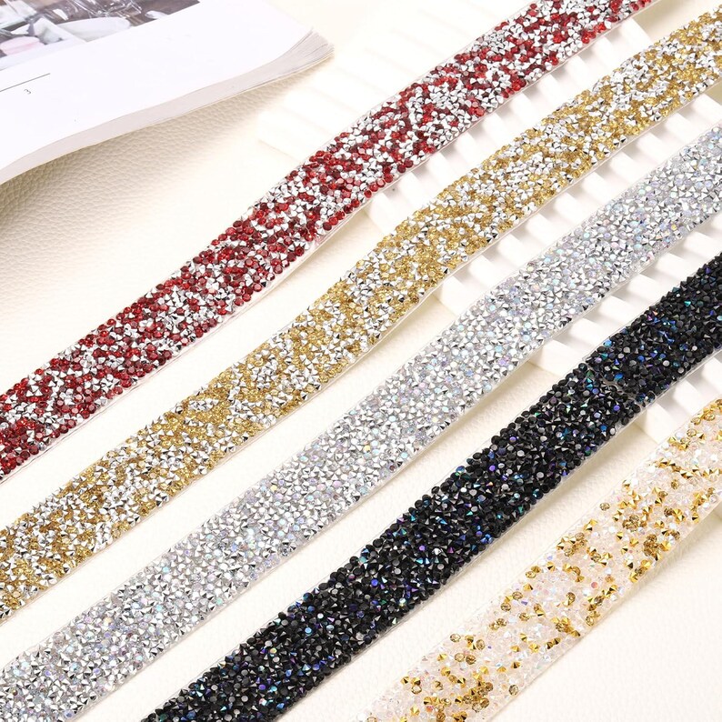 May include: Five parallel strips of decorative trim, each covered in small, reflective rhinestones. The colors include red, gold, silver, black, and a mix of white and gold. Each strip features a dense, uniform arrangement of faceted stones.