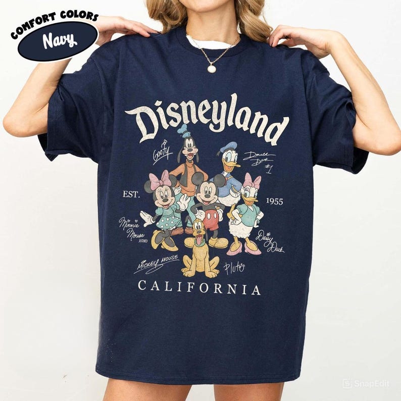 K&ouml;nnte beinhalten: Marineblaues T-Shirt mit dem Wort "Disneyland" in einer Vintage-Schriftart sowie Zeichentrickfiguren wie Micky Maus, Minnie Maus und Goofy. Das Shirt enth&auml;lt auch den Text "EST. 1955" und "CALIFORNIA".