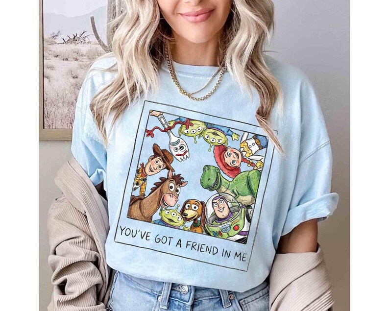 Puede incluir: Camiseta azul claro con un gr&aacute;fico colorido de personajes de la pel&iacute;cula animada "Toy Story". El gr&aacute;fico incluye a Woody, Buzz Lightyear y otros personajes. El texto "YOU'VE GOT A FRIEND IN ME" est&aacute; impreso debajo.