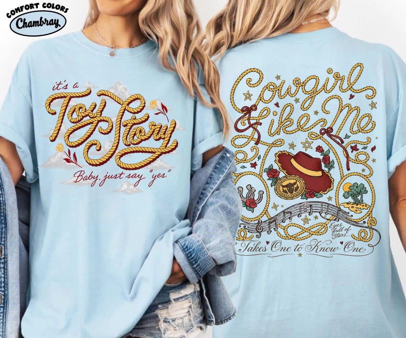 May include: A light blue t-shirt featuring a front graphic with yellow rope lettering that reads "it's a Toy Story Baby, just say "yes"". The back graphic displays "Cowgirl like Me" in rope text, a cowboy hat, a belt buckle, and musical notes.