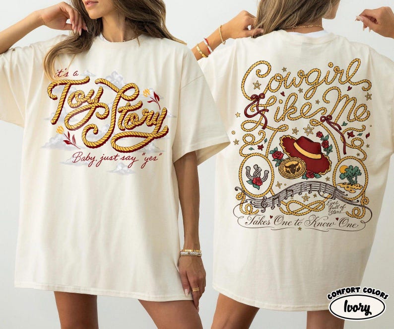 May include: An ivory t-shirt featuring a graphic print on the front and back. The front displays the text "it's a Toy Story Baby, just say "yes"" in rope-style lettering. The back features "Cowgirl like Me" and "Takes One to Know One" text.