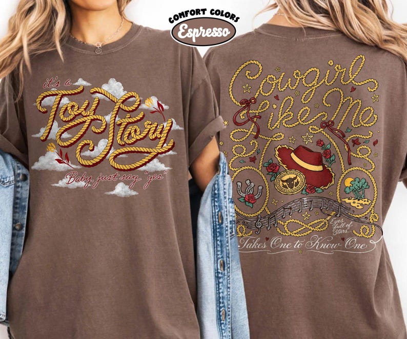 May include: An espresso-colored t-shirt featuring a front graphic with the text 'it's a Toy Story' in rope-style lettering over clouds. The back graphic displays 'Cowgirl like me' in rope text, a cowboy hat, a horseshoe, and musical notes.